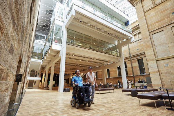 Man who uses a wheelchair and friend in Hintze Hall